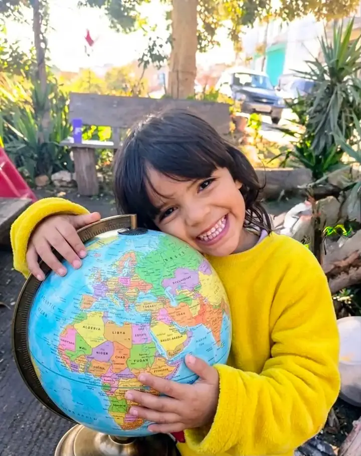 Menina sorrindo segurando um globo terrestre, representando a rede de apoio do Alerta Anjo